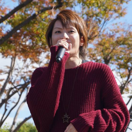 外で笑顔で歌を歌う上松さんの写真
