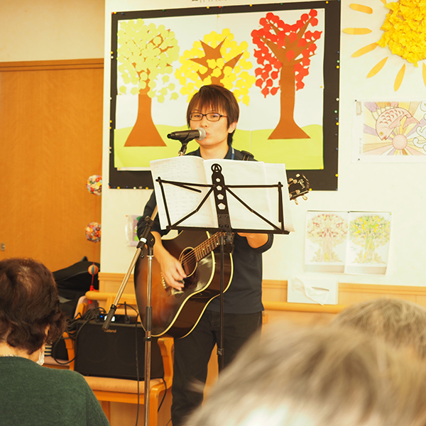 利用者さまの前で歌いながらギターを演奏する上松さん