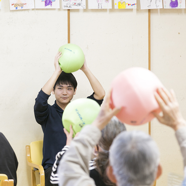 利用者さまと一緒にボールを用いて体操を行う森兼さんの写真