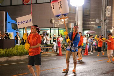 社名プレートと盆提灯を掲げて大通りを行進