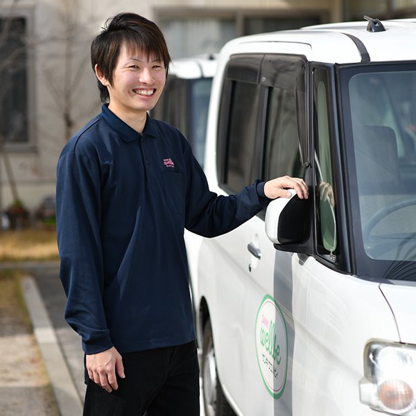 送迎車の横で笑顔を見せる上松さんの写真